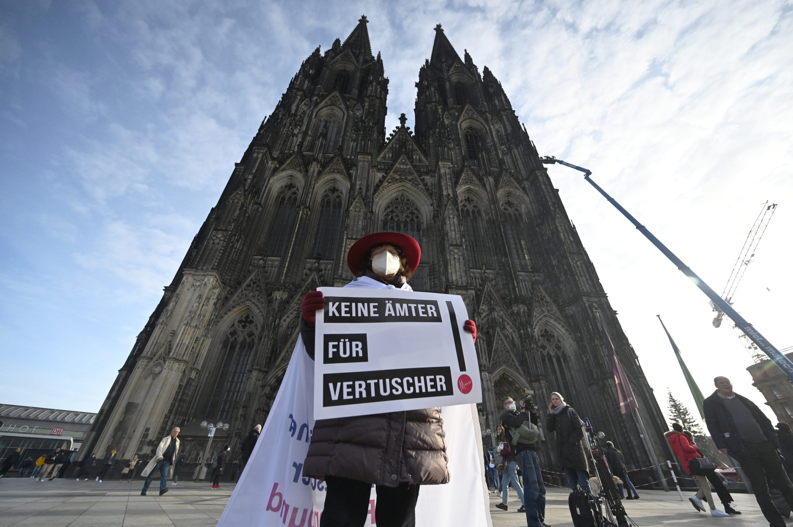 A participant of a rally of the initiative Maria 2.0 holds a poster with the inscription 'No offices for cover-ups' in front of the cathedral in Cologne, Germany, Thursday, Nov. 18, 2021 before the beginning of a penitential service of the archdiocese of Cologne in the course of coming to terms with sexual violence. (Henning Kaiser/dpa via AP)