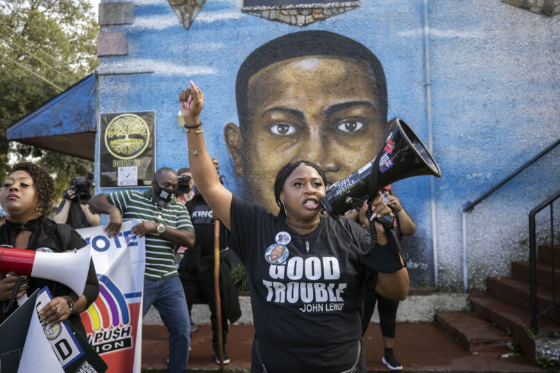 Civil rights activist Porchse Miller of Atlanta shouts into a megaphone in front of a mural of Ahmaud Arbery during march that followed the Wall of Prayer event outside the Glynn County Courthouse, Thursday, Nov. 18, 2021, in Brunswick, Ga. The Rev. Al Sharpton organized the event after defense attorney Kevin Gough to objected to the presence of Black pastors in the courtroom the trial for Arbery's killers. (AP Photo/Stephen B. Morton)
