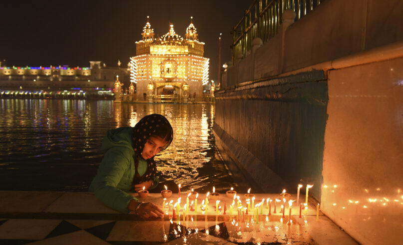 A Sikh devotee lights candles at the Golden Temple to mark the birth anniversary of Guru Nanak, the first Sikh Guru, in Amritsar, India, Friday, Nov. 19, 2021. (AP Photo/Prabhjot Gill)