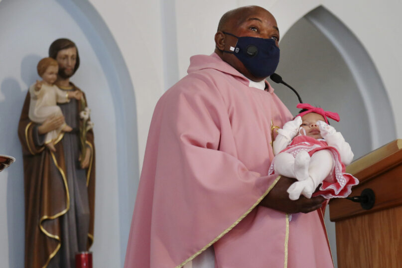 The Rev. Athanasius Abanulo introduces newborn Nathalia Perez to the congregation at Immaculate Conception Catholic Church on Dec. 12, 2021, in Wedowee, Alabama. Originally from Nigeria, Abanulo is one of numerous international clergy helping ease a U.S. priest shortage by serving in Catholic dioceses across the country. (AP Photo/Jessie Wardarski)