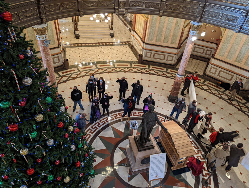 The Satanic Temple Illinois supporters, top center, surround a baby Baphomet, center, holiday display in the Illinois Statehouse rotunda in Springfield, Illinois, Dec. 20, 2021. Catholic protesters are on the right. Photo by Sharper for the Satanic Temple Illinois