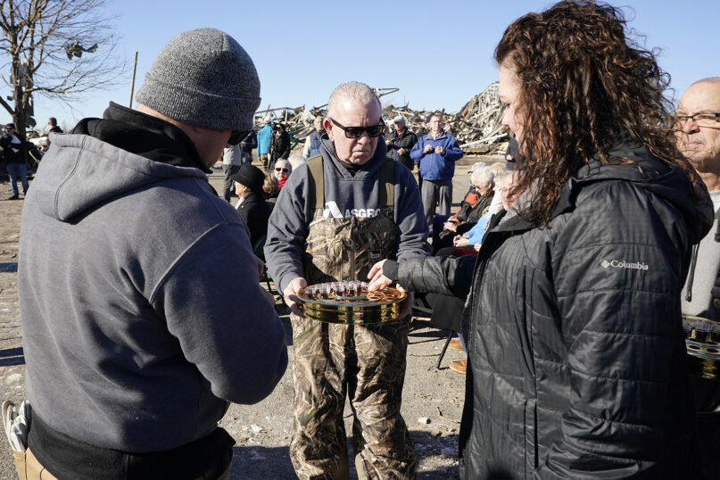Jim Heath, center, an elder with First Christian Church, serves communion during a service held in the church's parking lot Sunday, Dec. 12, 2021, in Mayfield, Ky. Members of three churches whose buildings were heavily damaged in Friday's storm joined together for a service. Tornadoes and severe weather caused catastrophic damage across several states Friday, killing multiple people. (AP Photo/Mark Humphrey)