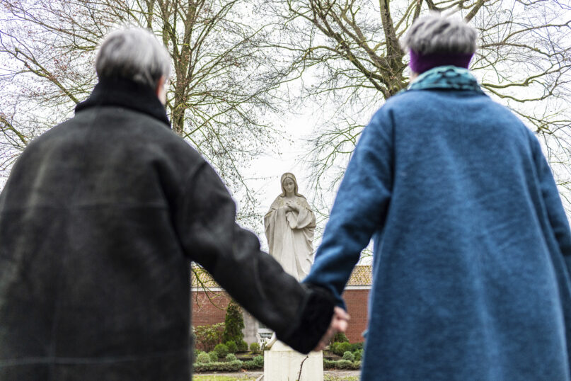 Monika Schmelter, left, and Marie Kortenbusch, right, stand hand in hand in front of a statue of Mary at a convent in Luedinghausen, Germany, Monday, Jan. 24, 2022. More than 100 employees of the Catholic Church in Germany publicly outed themselves as queer on Monday, saying they want to “live openly without fear