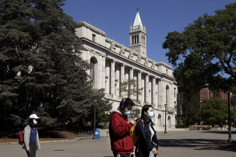 In this March 11, 2020, file photo, people wear masks while walking past Wheeler Hall on the University of California campus in Berkeley, California. California State University is the largest four-year public university system in the nation. (AP Photo/Jeff Chiu, File)