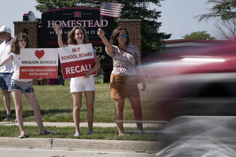 Supporters to recall the entire Mequon-Thiensville School District board wave at cars outside Homestead High School, Aug. 23, 2021, in Mequon, Wisconsin. A loose network of conservative groups with ties to major Republican donors and party-aligned think tanks is quietly lending firepower to local activists engaged in the culture war fights in schools across the country. (AP Photo/Morry Gash)
