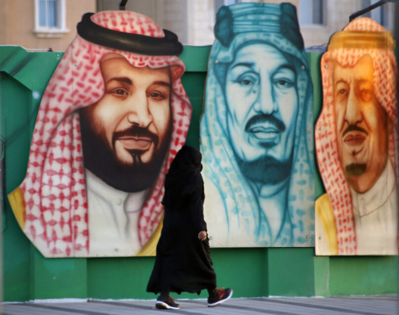 A woman walks in front of a banner showing Saudi King Salman, right, his Crown Prince Mohammed bin Salman, left, and Saudi Arabia's founder late King Abdul Aziz Al Saud in Dammam, in the Kingdom's Eastern Province, Saturday, June 26, 2021. (AP Photo/Amr Nabil)