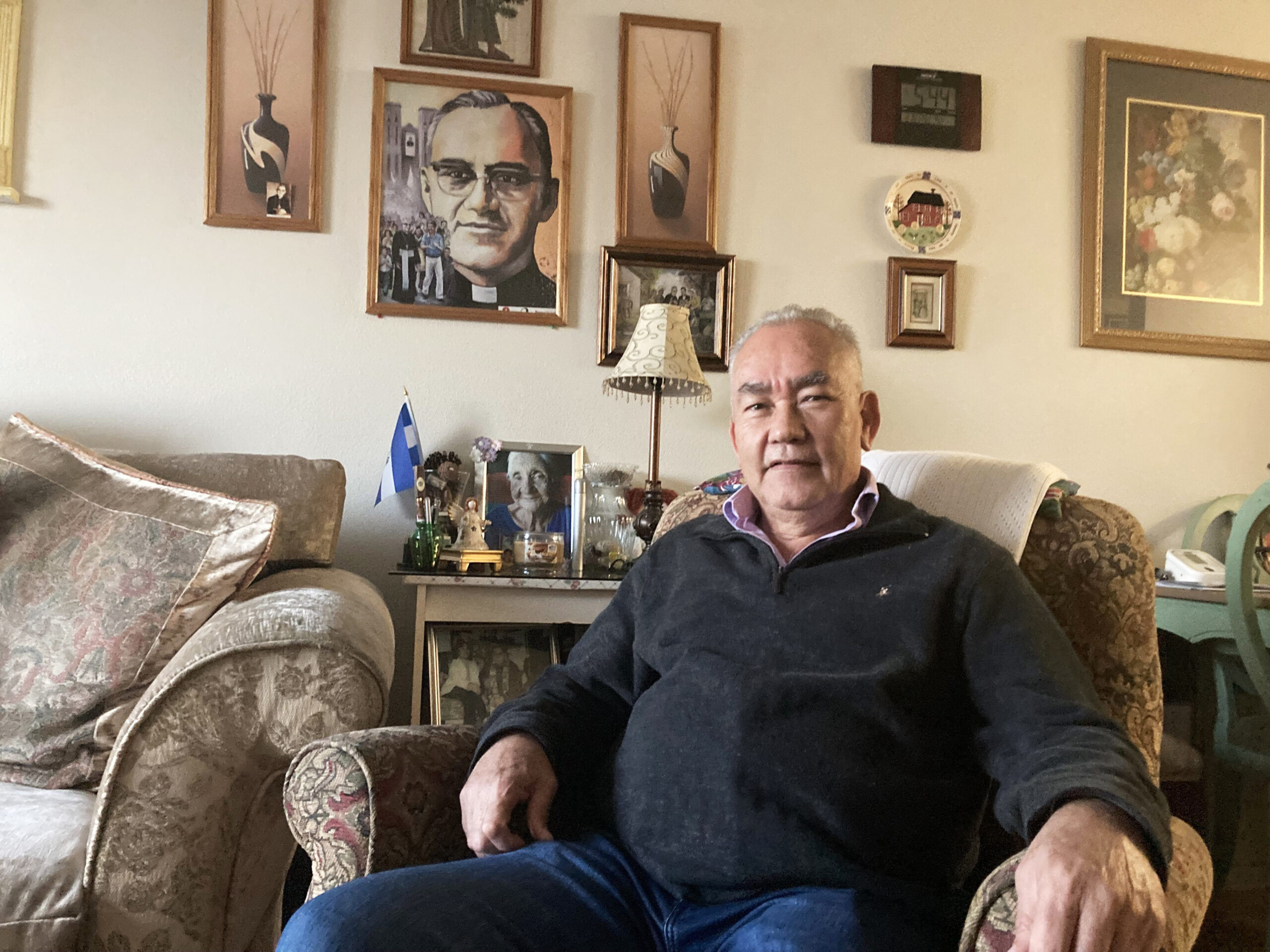 Jesœs Aguilar, de 65 a–os, se sienta para un retrato en su casa en Los çngeles, frente a una imagen de San Oscar Romero. RNS foto por Alejandra Molina