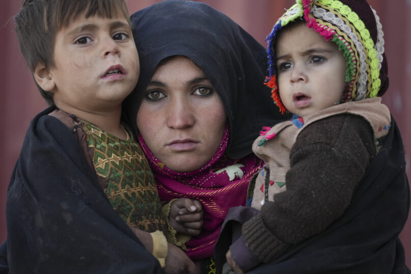 An Afghan woman holds her children as she waits for a consultation outside a makeshift clinic at a sprawling settlement of mud brick huts housing those displaced by war and drought near Herat, Afghanistan, Dec. 16, 2021. (AP Photo/Mstyslav Chernov, File)