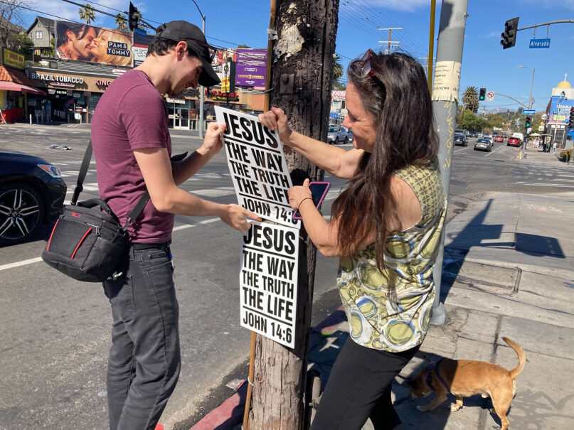 Evan Clark, left, and Christine Jones of Atheists United take down illegally placed religious materials from public streets in Los Angeles, Feb. 19, 2022. RNS photo by Alejandra Molina