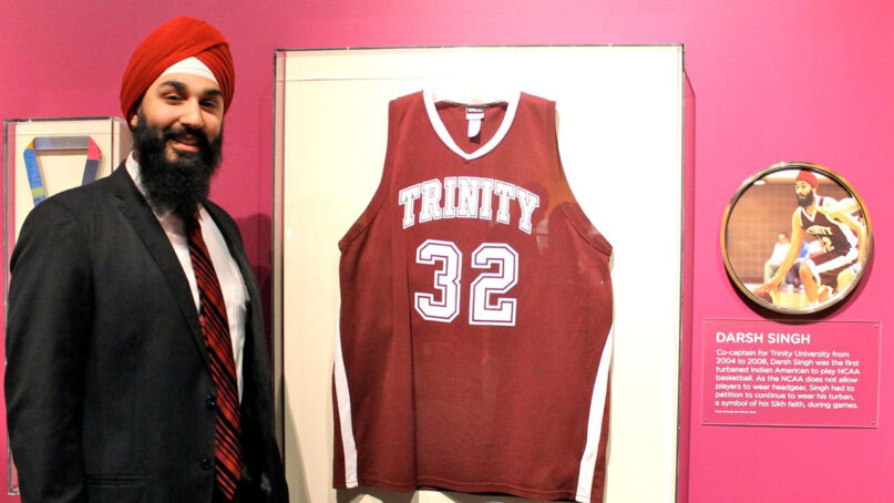 Darsh Preet Singh stands next to his college basketball jersey on display at the Smithsonian's National Museum of Natural History, part of an exhibition on Indian Americans, in 2014. Singh is the first Sikh American to play basketball in the NCAA while wearing his turban. Photo by Lakhpreet Kaur