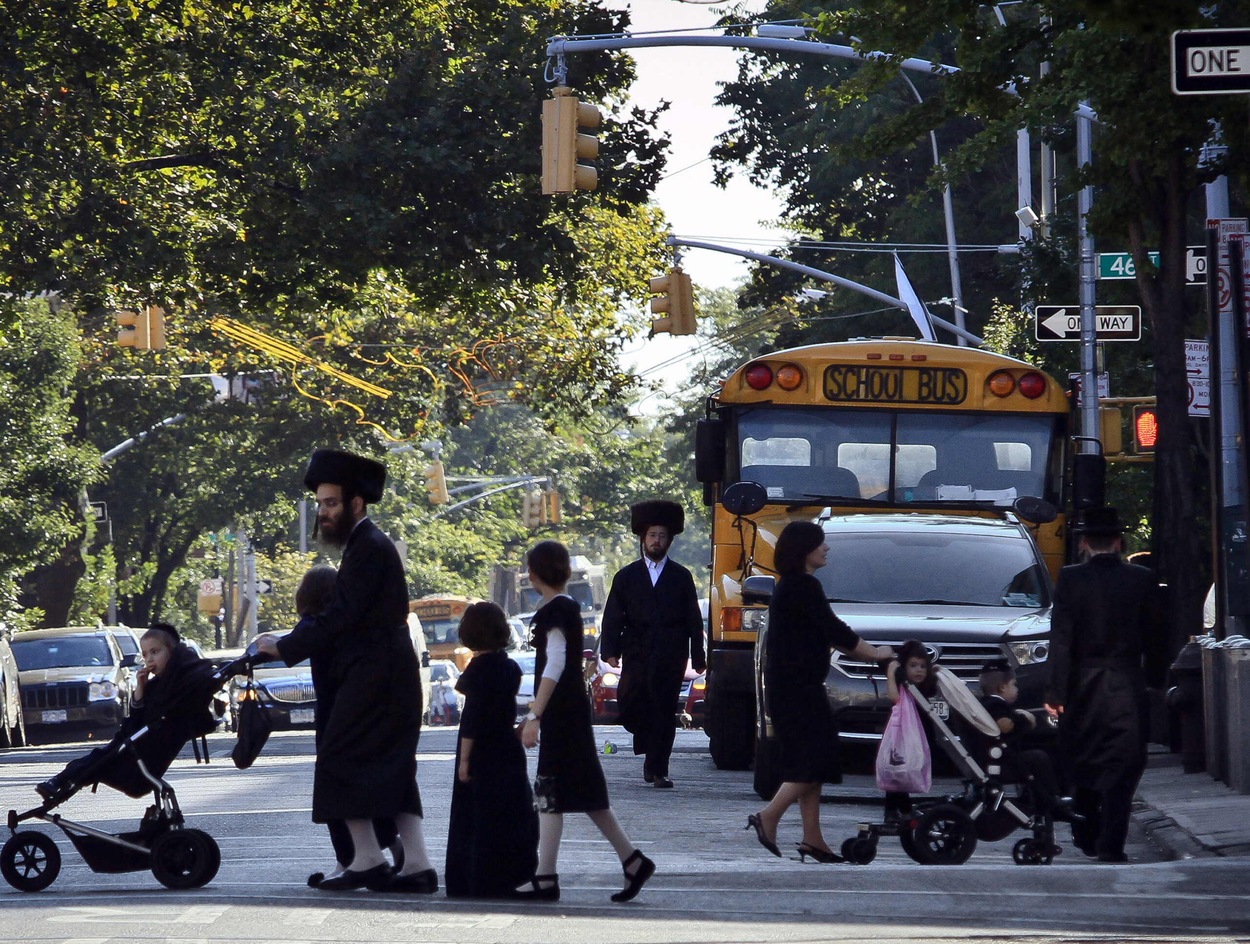FILE - In this Sept. 20, 2013 file photo, children and adults cross a street in front of a school bus in Borough Park, a neighborhood in the Brooklyn borough of New York that is home to many ultra-Orthodox Jewish families. Critics have charged for years that the rudimentary level of secular education at private yeshiva schools serving New York's Hasidic communities are deficient in teaching science, geography and math to grade school students. Now, for the first time, the city Department of Education is investigating more than three dozen of the schools to make sure their instruction is up to the most basic standards. (AP Photo/Bebeto Matthews, File)
