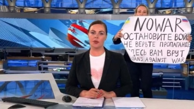 A video screen grab shows Russian Channel One editor Marina Ovsyannikova, right, holding a poster protesting the war during a live evening news broadcast, in Moscow, March 14, 2022. Video screen grab