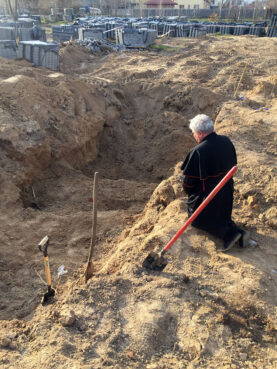 Cardinal Konrad Krajewski, the papal almoner, prays next to a mass grave in Ukraine. Photo by Vatican Media