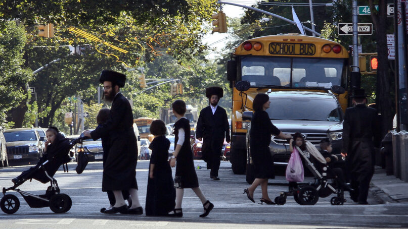 In this Sept. 20, 2013, file photo, children and adults cross a street in front of a school bus in Borough Park, a neighborhood in the Brooklyn borough of New York that is home to many ultra-Orthodox Jewish families. (AP Photo/Bebeto Matthews, File)