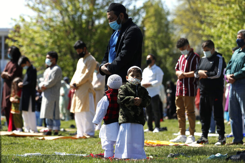 Two children stand with their father as he and other Muslims perform an Eid al-Fitr prayer in an outdoor open area, marking the end of the fasting month of Ramadan, May 13, 2021, in Morton Grove, Illinois. (AP Photo/Shafkat Anowar)