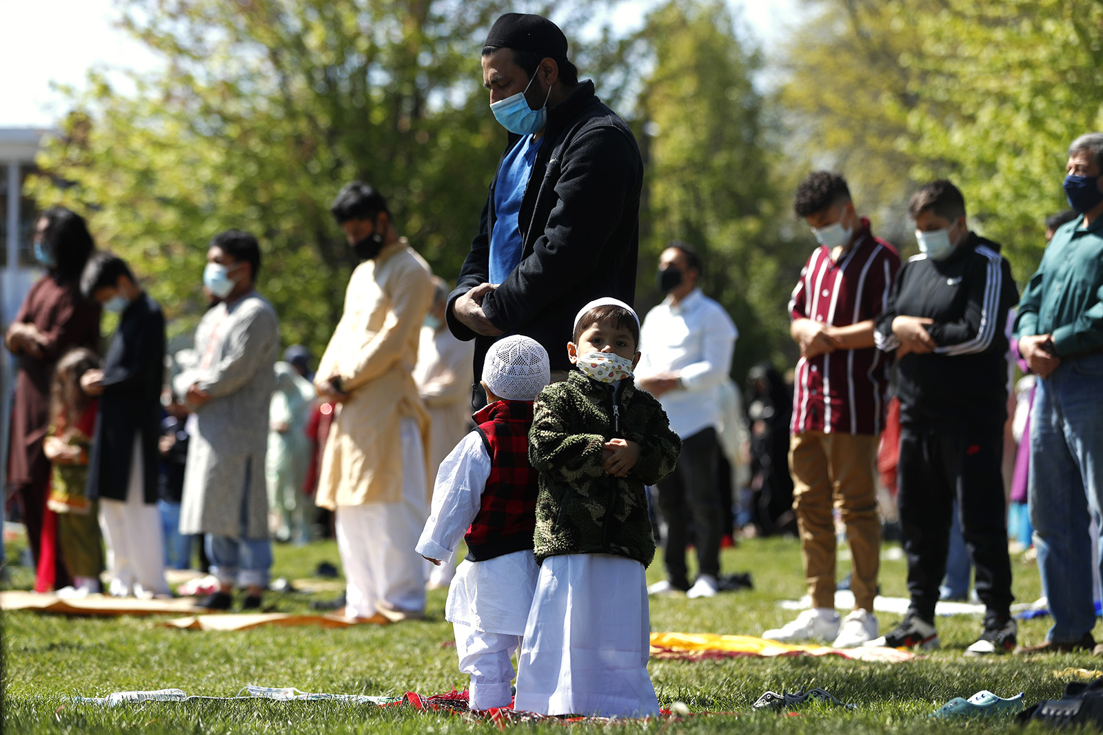 Two children stand with their father as he and other Muslims perform an Eid al-Fitr prayer in an outdoor open area, marking the end of the fasting month of Ramadan, May 13, 2021, in Morton Grove, Illinois. (AP Photo/Shafkat Anowar)