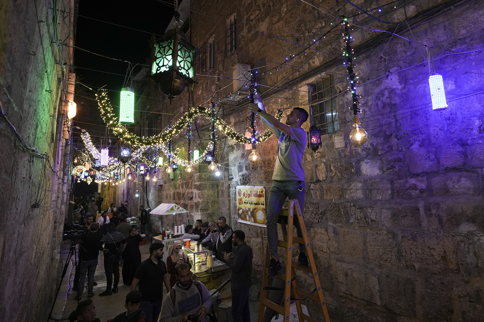 A Palestinian man hangs decorative lights in preparation for the holy Muslim month of Ramadan, at the streets of Jerusalem's Old City, Friday, April 1, 2022. (AP Photo/Mahmoud Illean)
