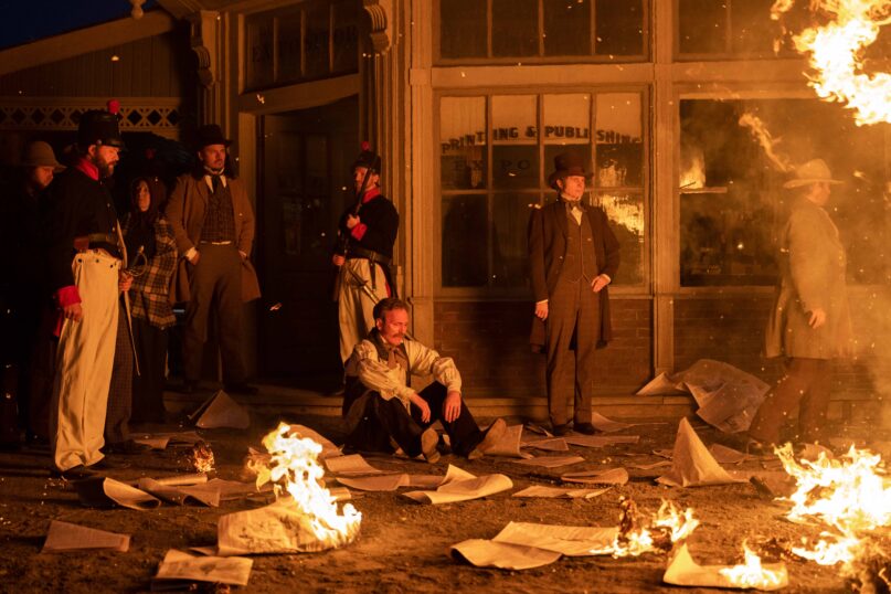 Hyrum Smith (Andrew David Long), right,  causes a fire at the publishing house of William Law (Tom Carey), seated, in an episode of “Under the Banner of Heaven.” Photo by Michelle Faye/FX
