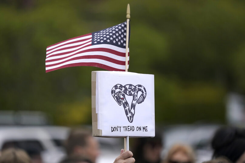 A person holds a sign that reads “Don’t Tread On Me” with a uterus-shaped snake and an American flag, May 3, 2022, during a rally at a park in Seattle in support of abortion rights. (AP Photo/Ted S. Warren)