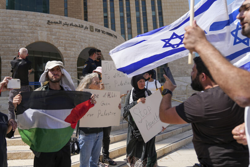 Supporters of Mohammad El Halabi hold a Palestinian flag and placards as protesters wave Israeli flags outside the district court in the southern Israeli city of Beersheba, June 15, 2022. The court found the Gaza aid worker guilty of several terrorism charges. El Halabi, who was the Gaza director for the Christian charity World Vision from 2014 until his arrest in 2016, was accused of diverting tens of millions of dollars to the Islamic militant group Hamas that rules the territory. Both El Halabi and World Vision have denied any wrongdoing, and an independent audit in 2017 also found no evidence of support for Hamas. (AP Photo/Tsafrir Abayov)