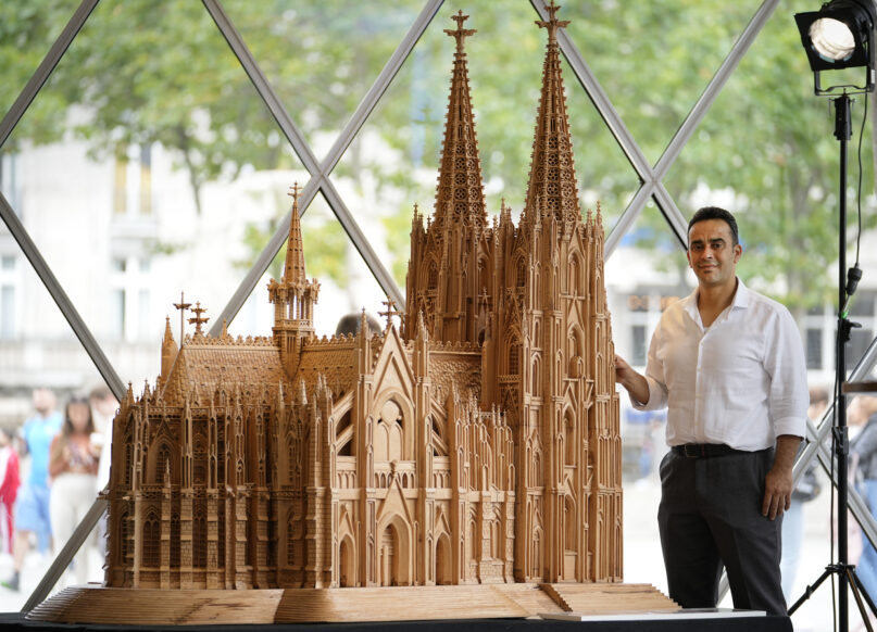 Fadel Alkhudr from Syria poses beside his wooden model of the word heritage Cologne Cathedral on display at the Domforum in Cologne, Germany, Monday, June 20, 2022. Fadel Alkhudr, 42, a woodcarver and artist orginally from Aleppo, Syria, fled the war in his home country and arrived in the western german city of Cologne in 2015. In 2019 he started to carve the local Cologne Cathedral in his small basement - without any plans or drawings, using only cell phone photos of the cathedral as a template. (AP Photo/Martin Meissner)