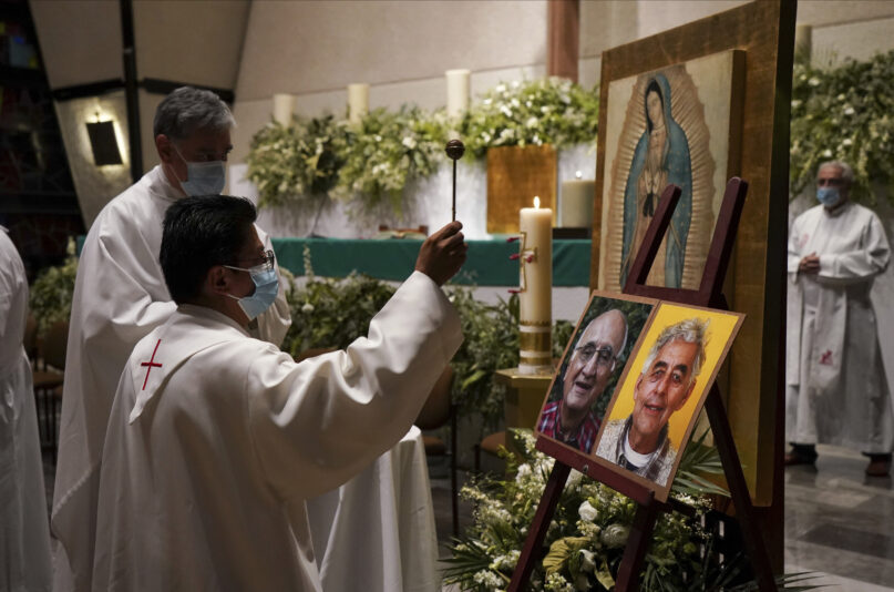 A priest blesses the photos of Jesuit priests Javier Campos Morales, left, and Joaquin Cesar Mora Salazar during a Mass to mourn them, at a church in Mexico City, Tuesday, June 21, 2022. The two elderly priests were killed inside a church where a man pursued by gunmen apparently sought refuge in a remote mountainous area of northern Mexico, the religious order’s Mexican branch announced Tuesday. (AP Photo/Fernando Llano)
