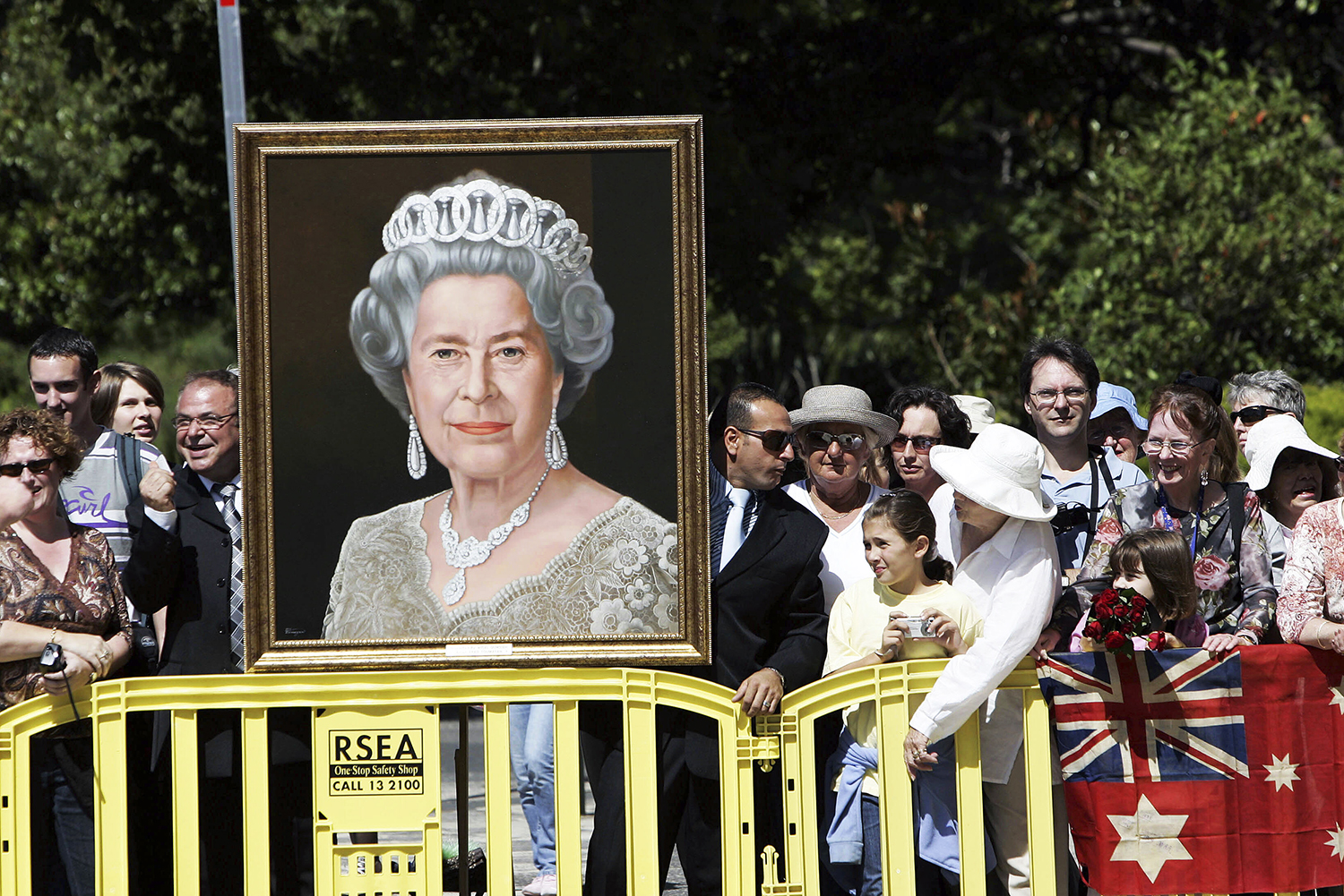 FILE - Wellwishers holding a portrait of Britain's Queen Elizabeth II wait for her arrival in Melbourne, Australia, Wednesday March 15, 2006. After seven decades on the throne, Queen Elizabeth II is widely viewed in the U.K. as a rock in turbulent times. But in Britain’s former colonies, many see her as an anchor to an imperial past whose damage still lingers. (AP Photo/Rick Stevens, File)