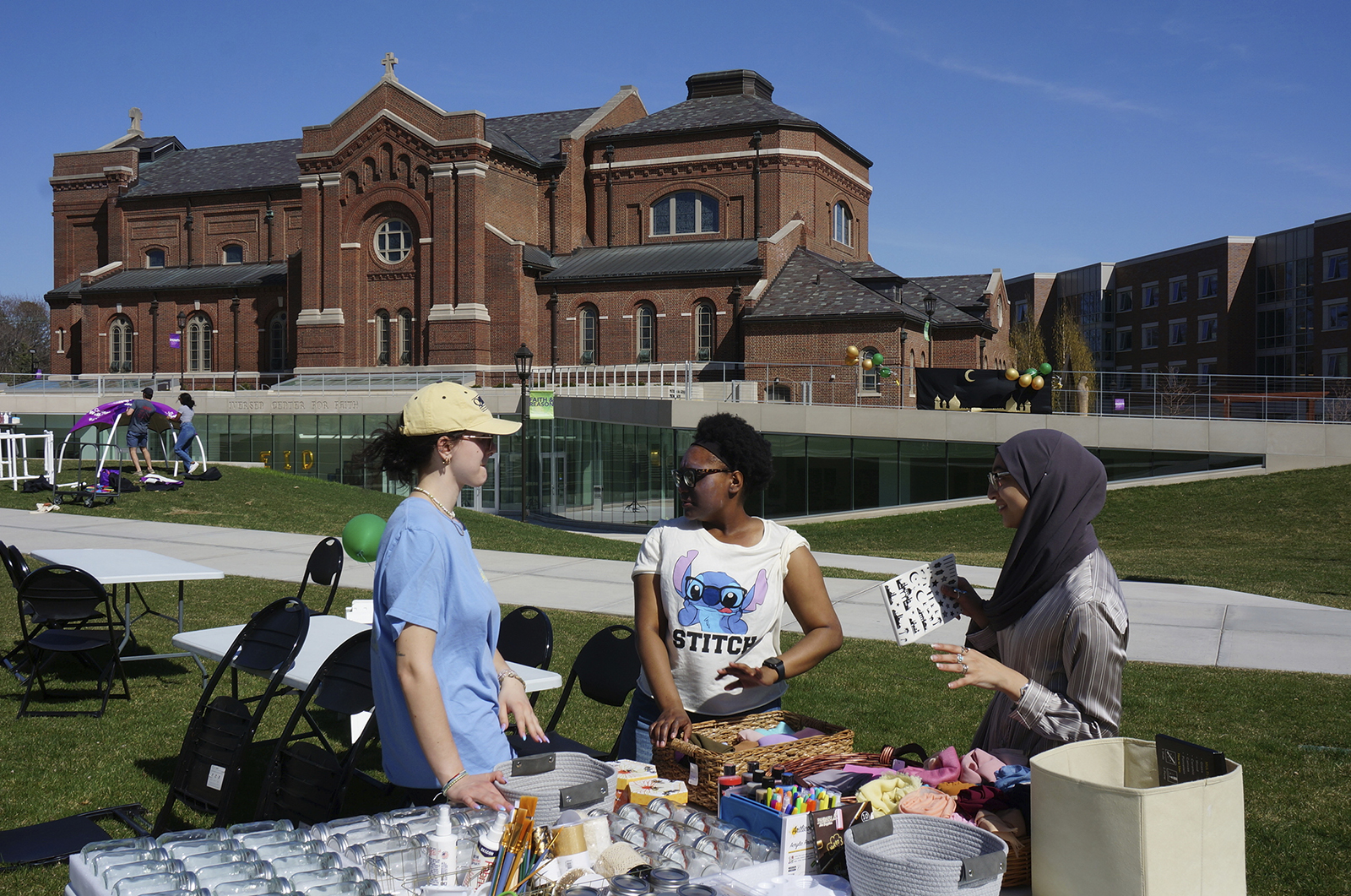 From left, University of St. Thomas students Helen Knudson, Arianna Norals, and Salma Nadir set up a table for decorating mason jars and headscarves at the school's celebration for the end of the Muslim holy month of Ramadan on the lawn in front of the Catholic chapel in St. Paul, Minn., on Saturday, May 7, 2022. Campus ministry helped organize the event, which included similar stress-reducing activities, as many faith leaders across US campuses seek ways to help students manage stress and anxiety. (AP Photo/Giovanna Dell'Orto)