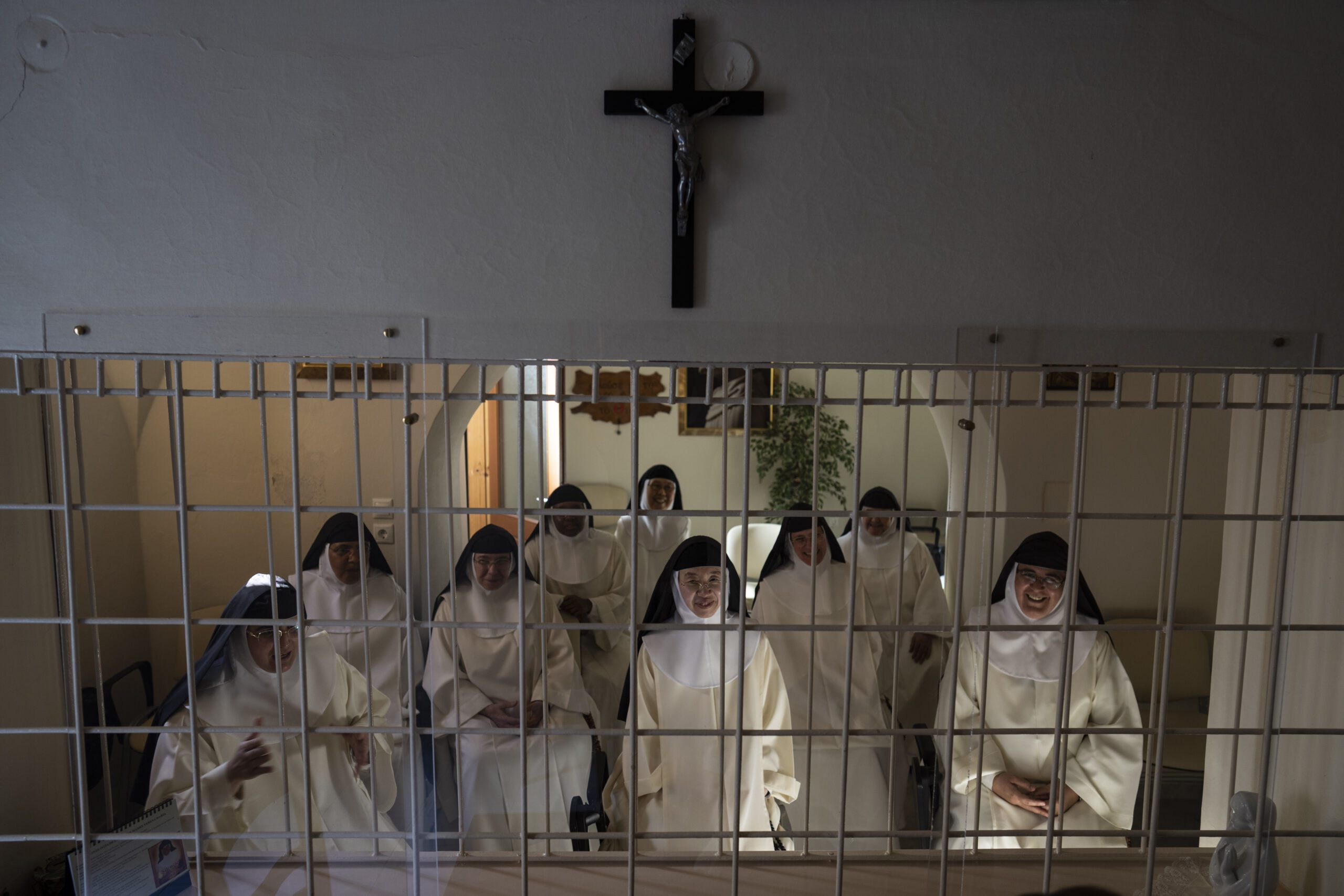 Nuns speak to journalists from behind a white iron grille in the parlor of the Monastery of St. Catherine on the Greek island of Santorini on Tuesday, June 14, 2022. In the first row, from right to left, are Sister Lucía María de Fátima, the prioress, Sister María de la Trinidad, and Sister María Guadalupe. The convent is home to more than a dozen nuns who devote themselves to prayer and leave only for medical or government necessities. (AP Photo/Petros Giannakouris)