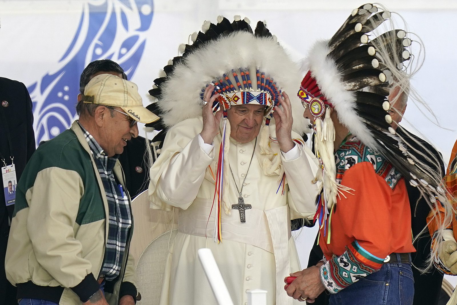 Pope Francis puts on an Indigenous headdress during a meeting with Indigenous communities, including First Nations, Métis and Inuit, at Our Lady of Seven Sorrows Catholic Church in Maskwacis, near Edmonton, Canada, Monday, July 25, 2022. Pope Francis begins a "penitential" visit to Canada to beg forgiveness from survivors of the country's residential schools, where Catholic missionaries contributed to the "cultural genocide" of generations of Indigenous children by trying to stamp out their languages, cultures and traditions. Francis is set to visit the cemetery at the former residential school in Maskwacis. (AP Photo/Eric Gay)