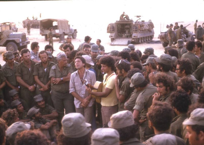 Leonard Cohen, center left, performs for IDF troops in the Sinai during the Yom Kippur War in 1973. General Ariel Sharon is to the left of Cohen. Israeli pop singer Matti Caspi plays the guitar. (IDF Archives)