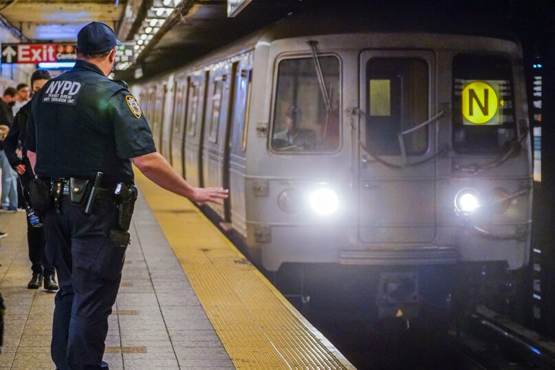 As a subway train enters the Canal Street Q and N station, a New York Police Department transit officer from the anti-terrorism unit gestures to the driver, May 24, 2022, in New York. (AP Photo/Mary Altaffer)
