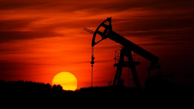 The sun sets behind a pumpjack at an oil well. Photo by Zbynek Burival/Unsplash/Creative Commons