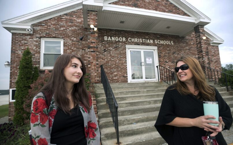Former Bangor Christian Schools sophomore Olivia Carson, then 15, of Glenburn, Maine, left, stands with her mother Amy while getting dropped off on the first day of school on August 28, 2018 in Bangor, Maine. Parents of students enrolled in religious schools fought for years — all the way to the Supreme Court — for tuition to be reimbursed by the state, the same as other private schools. But only one religious school has signed up to participate so far. (Gabor Degre/The Bangor Daily News via AP, File)