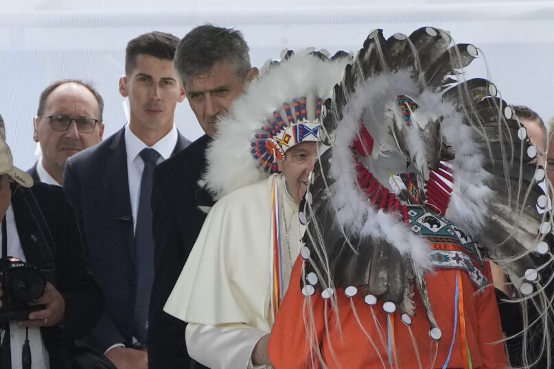 Massimiliano Strappetti, left, watches Pope Francis putting on an indigenous headdress during a meeting with indigenous communities, including First Nations, Metis and Inuit, at Our Lady of Seven Sorrows Catholic Church in Maskwacis, Canada, Monday, July 25, 2022. Francis has promoted the Vatican nurse whom he credited with saving his life to be his 