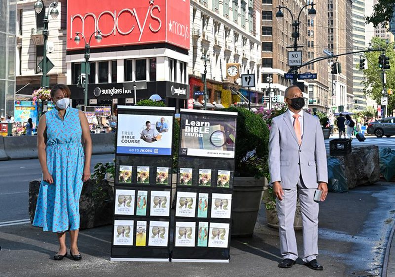 Elizabeth and Mark Godoy pose beside a display of Bible-based literature in Herald Square in New York City. Photo courtesy of Jehovah's Witnesses