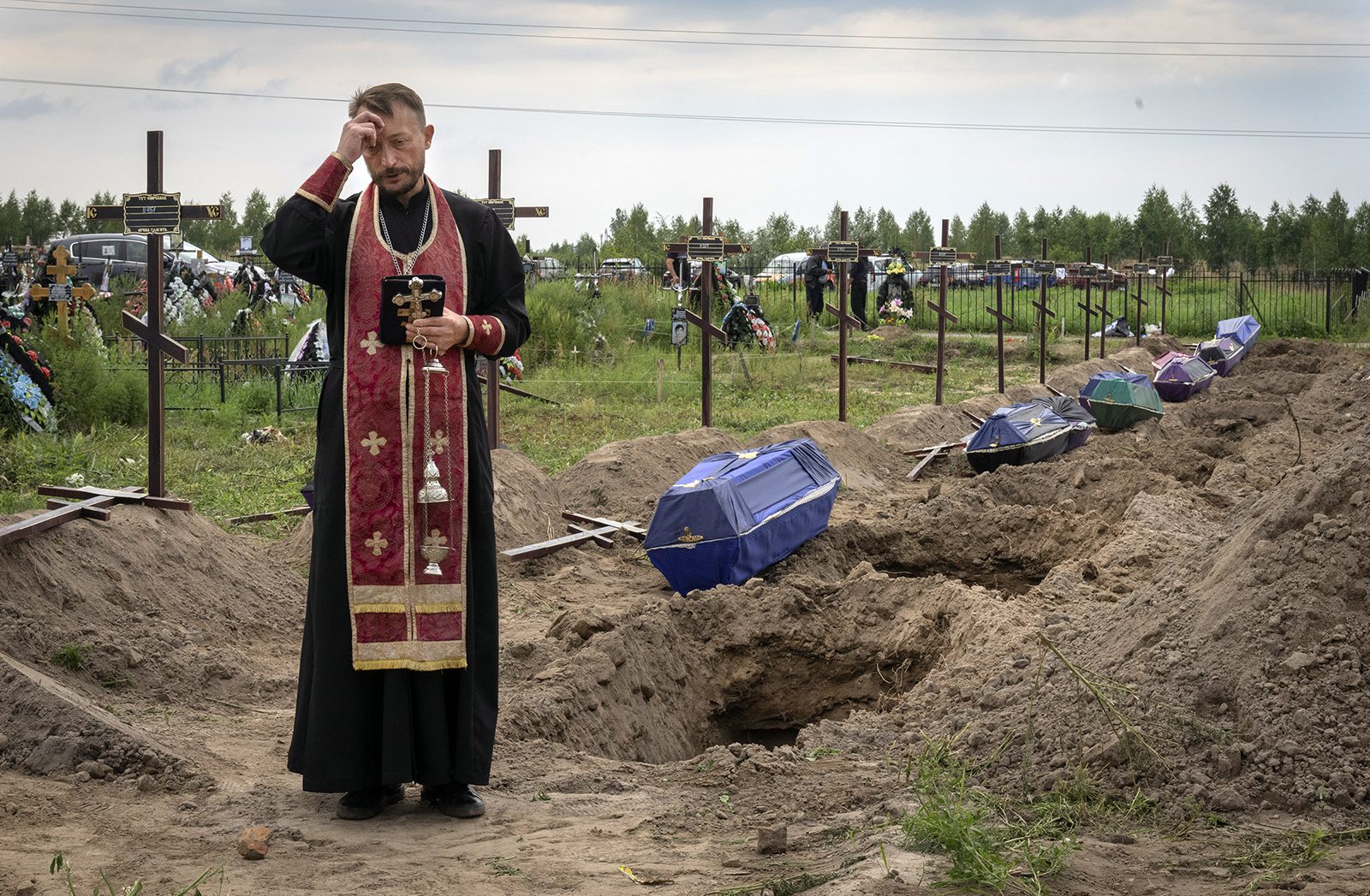 A priest prays for unidentified civilians killed by Russian troops during Russian occupation in Bucha, on the outskirts of Kyiv, Ukraine, Aug. 11, 2022. Eleven unidentified bodies exhumed from a mass grave were buried in Bucha Thursday. (AP Photo/Efrem Lukatsky)