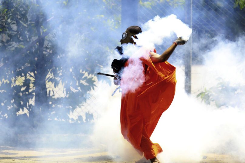 A man dressed as a Buddhist monk throws back a tear gas canister after it was fired by police to disperse protesters in Colombo, Sri Lanka, July 9, 2022. Sri Lankan protesters demanding that President Gotabaya Rajapaksa resign forced their way into his official residence as thousands of people took to the streets in the capital decrying the island nation's worst economic crisis in recent memory. (AP Photo/Amitha Thennakoon)
