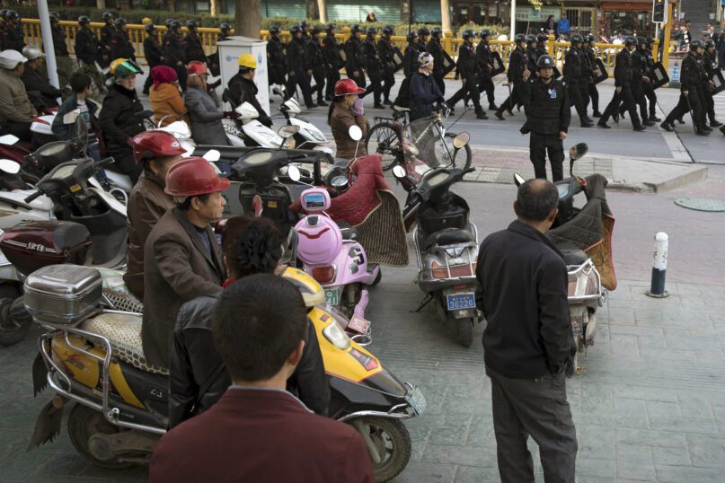Residents watch a convoy of security personnel armed with batons and shields patrol through central Kashgar in western China's Xinjiang region, Nov. 5, 2017. China's discriminatory detention of Uyghurs and other mostly Muslim ethnic groups in the western region of Xinjiang may constitute crimes against humanity, the U.N. human rights office said in a long-awaited report Aug. 31, 2022, which cited 