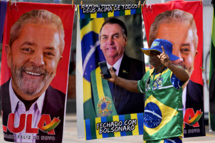 A demonstrator dressed in the colors of the Brazilian flag performs in front of a street vendor's towels for sale featuring Brazilian presidential candidates, current President Jair Bolsonaro, center, and former President Luiz Inacio Lula da Silva, in Brasilia, Brazil, Tuesday, Sept. 27, 2022. Nearly a dozen candidates are running in Brazil’s presidential election but only two stand a chance of reaching a runoff: former President Luiz Inacio Lula da Silva and incumbent Jair Bolsonaro. (AP Photo/Eraldo Peres)
