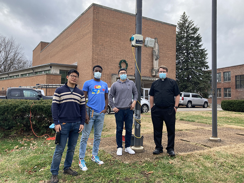 David Yeom, Intern with WashU, from left, Tyler Cargill, WashU PHD student with Jay Turner Lab, and Li Zhiyao, WashU PHD student Jay Turner Lab, work with Father Nick Winker to set up an air pollution monitor at St. Ann Catholic Church in St. Louis. Photo by Beth Gutzler