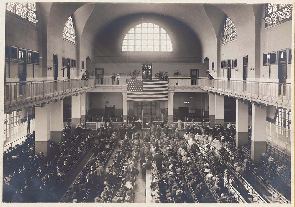 Immigrants seated on long benches at Ellis Island. Photo courtesy of New York Public Library