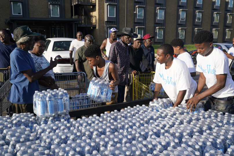 Residents of the Golden Keys Senior Living apartments flock to a trailer full of water being distributed by the AIDS Healthcare Foundation in Jackson, Miss., Thursday, Sept. 1, 2022. A recent flood worsened Jackson's long-standing water system problems. (AP Photo/Steve Helber)
