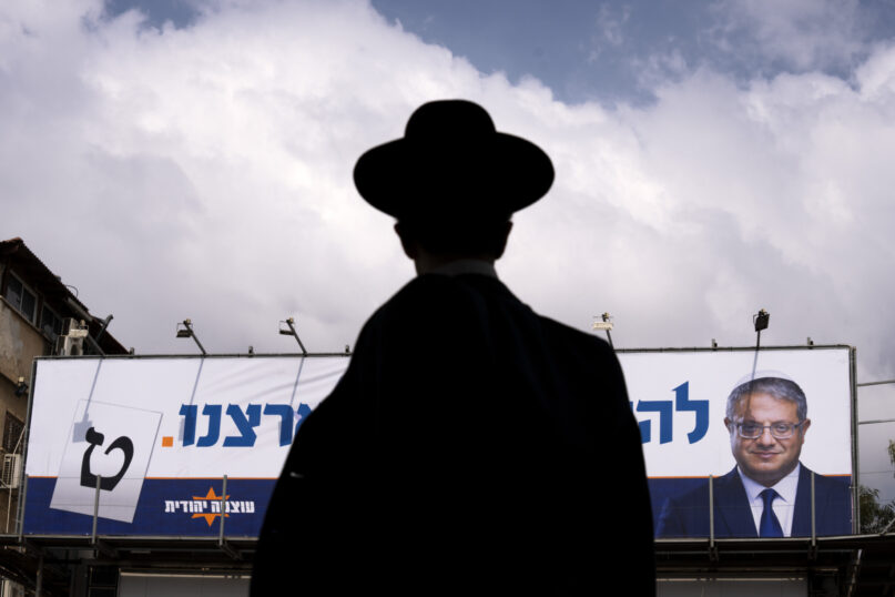 An ultra-Orthodox Jewish man walks by an election campaign billboard showing Itamar Ben-Gvir, Israeli far-right lawmaker and the head of 