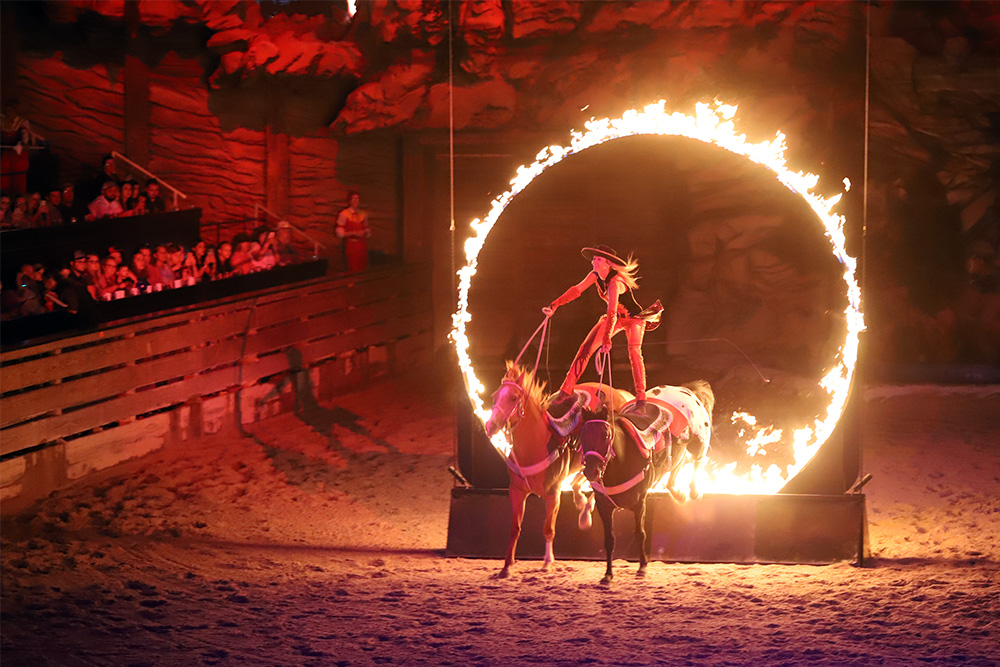 A woman rides horses through a ring of fire during Dolly Parton's Stampede dinner show on Aug. 26, 2022, in Branson, Mo. RNS photo by Kit Doyle