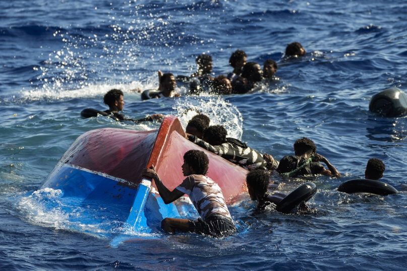 FILE - Migrants swim next to their overturned wooden boat during a rescue operation by Spanish NGO Open Arms, south of the Italian Lampedusa island in the Mediterranean Sea, Aug. 11, 2022. Multiple shipwrecks of migrant boats off Greece that left more than 20 people dead in August once again put the spotlight on the dangers of the Mediterranean migration route to Europe. (AP Photo/Francisco Seco, file)