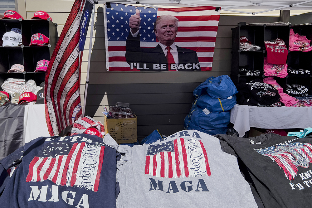 MAGA merchandise and a U.S. flag decorated with an image of former President Donald Trump that reads "I'll Be Back" are displayed for sale during the ReAwaken America tour at Cornerstone Church, in Batavia, N.Y., Saturday, Aug. 13, 2022. Michael Flynn, a retired three-star general who served as Trump's national security adviser, has drawn together election deniers, mask and vaccine opponents, insurrectionists, Proud Boys, and elected officials and leaders in state and local Republican parties. Along the way, AP and Frontline documented, Flynn and his companies have earned hundreds of thousands of dollars for his efforts. (AP Photo/Carolyn Kaster)