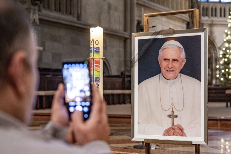 A person takes a picture of a portrait of Pope Emeritus Benedict XVI at St. Peter's Cathedral in Regensburg, Germany, Saturday, Dec. 31, 2022. Pope Emeritus Benedict XVI, the German theologian who will be remembered as the first pope in 600 years to resign, has died, the Vatican announced Saturday. He was 95. (Armin Weigl/dpa via AP)