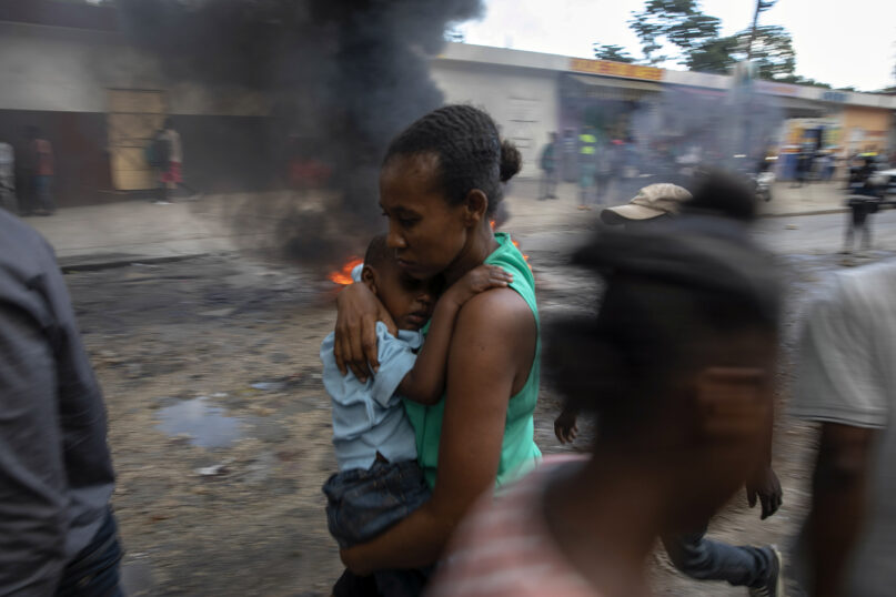 A mother carries her son as she runs past a burning barricade during a protest against the government in Port-au-Prince, Haiti, Friday, Nov. 18, 2022. (AP Photo/Odelyn Joseph)