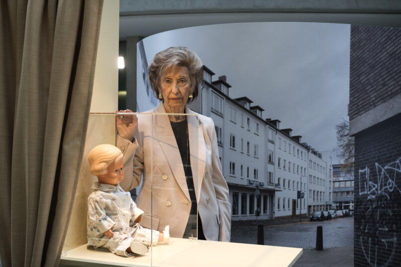 Holocaust survivor Lore Mayerfeld poses next to her doll 'Inge' as part of an exhibition with items from Israel's Yad Vashem Holocaust memorial in the German parliament Bundestag in Berlin, Germany, Monday, Jan. 23, 2023. An exhibition marking the 70th anniversary of Israel's Yad Vashem Holocaust memorial brings back to Germany a diverse set of everyday objects that Jews took with them when they fled the Nazis. (AP Photo/Markus Schreiber)